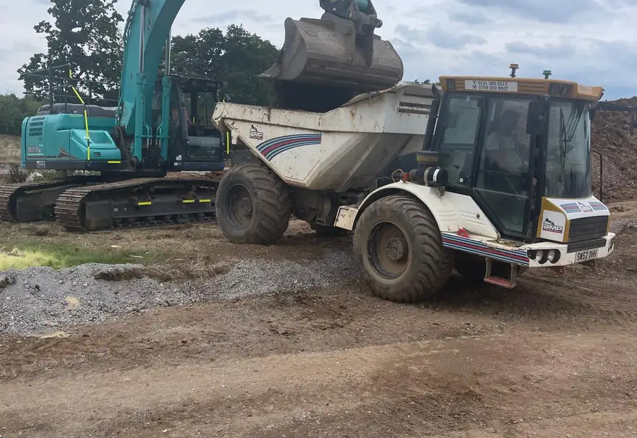 A tracked 360-degree excavator tipping a bucket of spoil into a site dumper